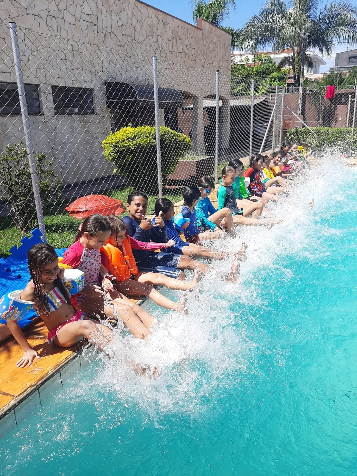 Crianças sentadas na borda da piscina batendo os pés na água