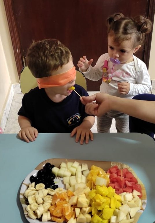 Menino de olhos vendados provando frutas